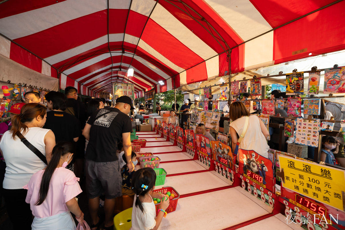 赤白テントの市集ブースで遊技ゲームを楽しむ来場者と子どもたち