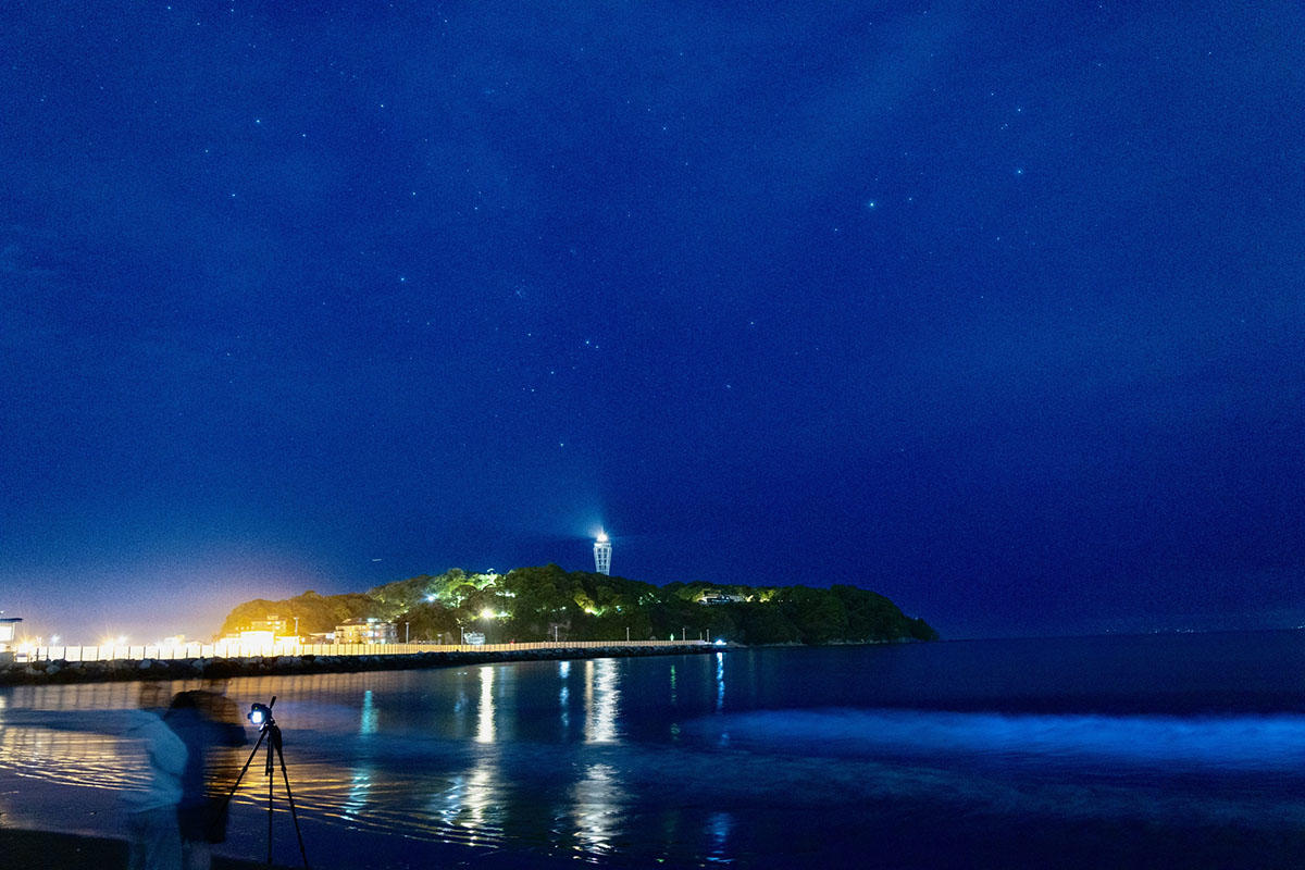 片瀬海岸西浜の夜光虫。三脚を構えるカメラマンと江ノ島の灯台